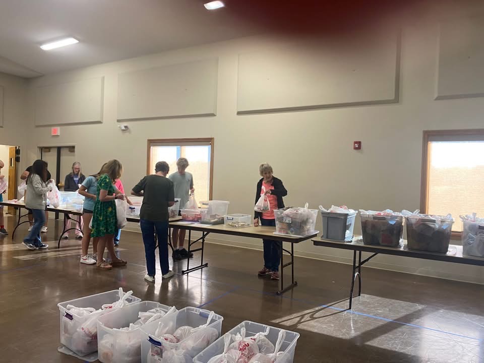 Volunteers packing food into care packs at tables in the community hall